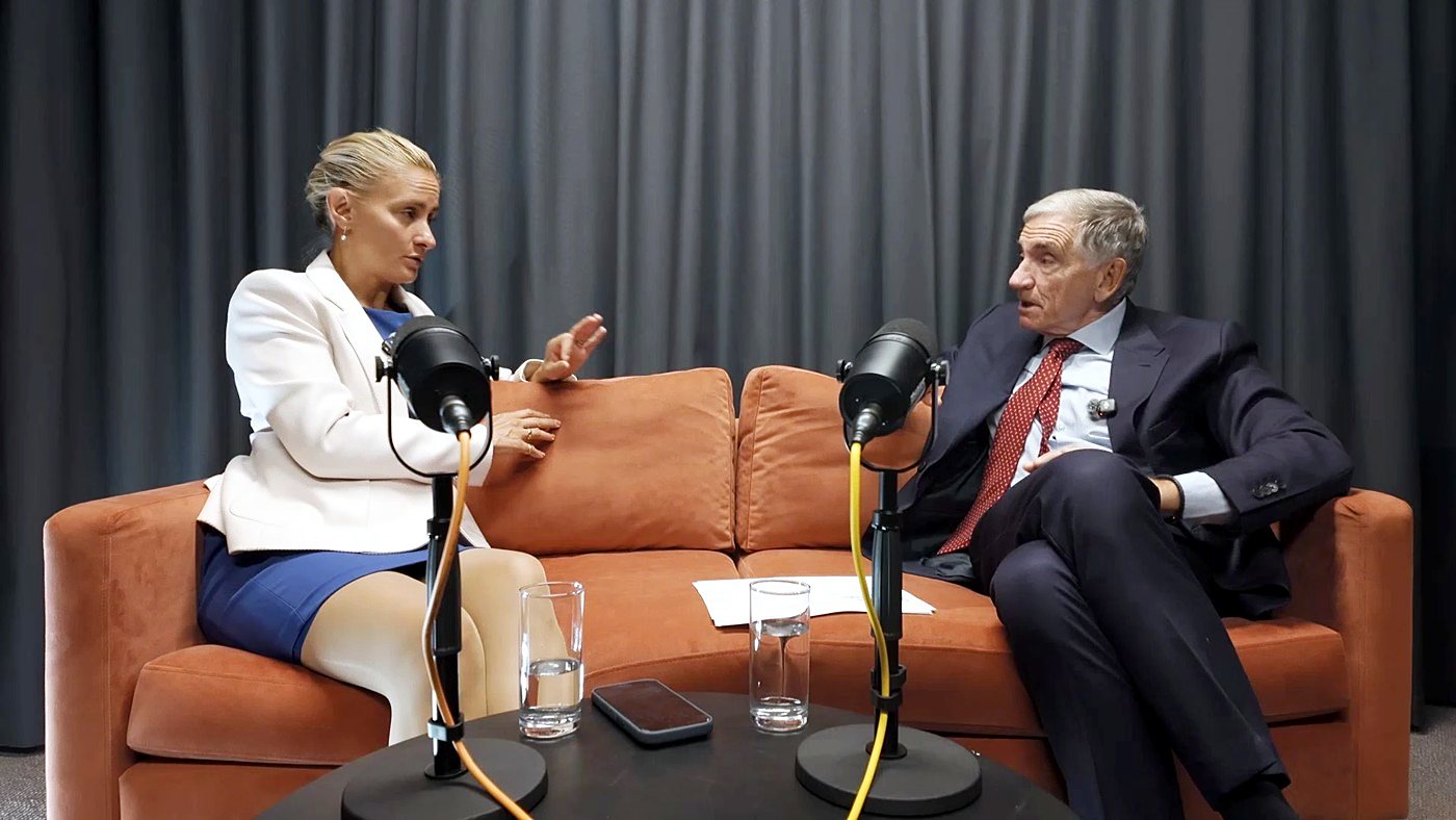 Two people in conversation on an orange sofa in The Dokkcast studio, with microphones in front of them