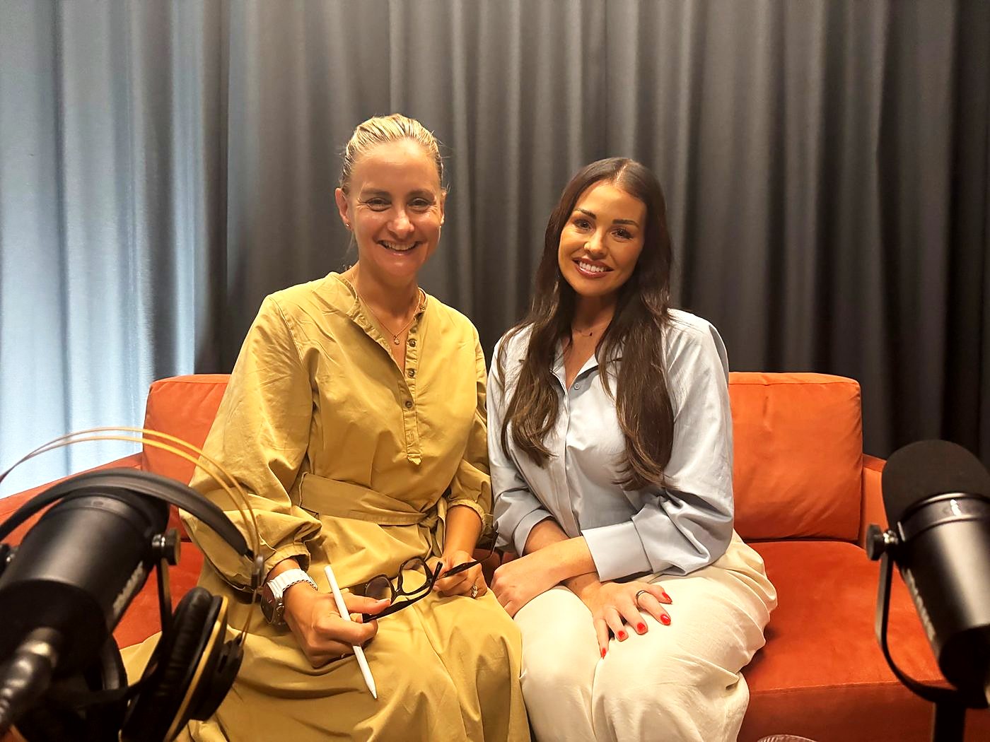 Two people smiling as they sit together on an orange sofa in The Dokkcast studio