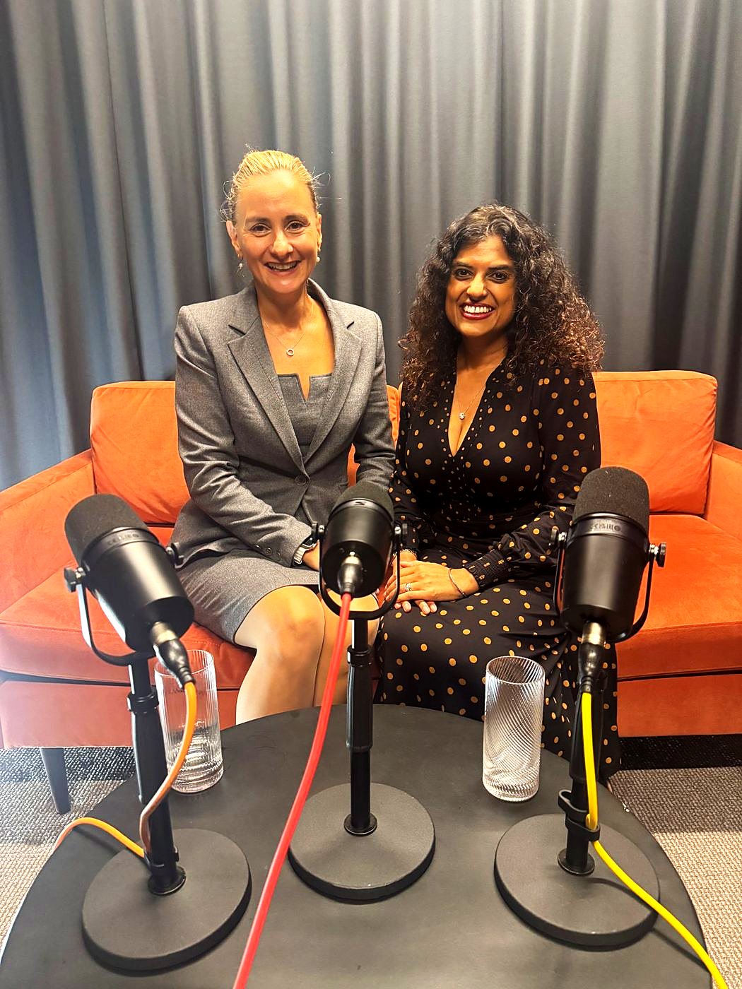 Two guests smiling on an orange sofa behind three microphones in The Dokkcast studio