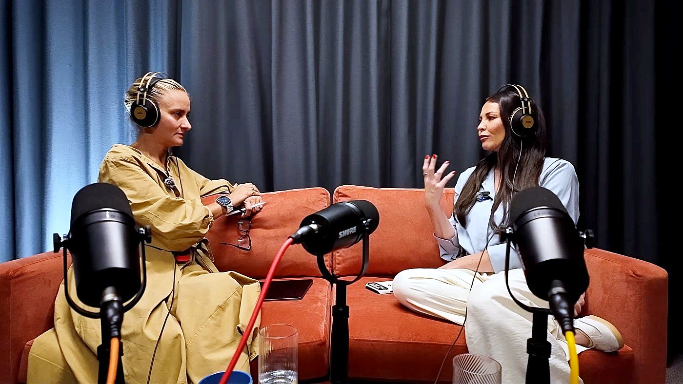 Two people wearing headphones in conversation on an orange sofa in The Dokkcast studio, with microphones in the foreground
