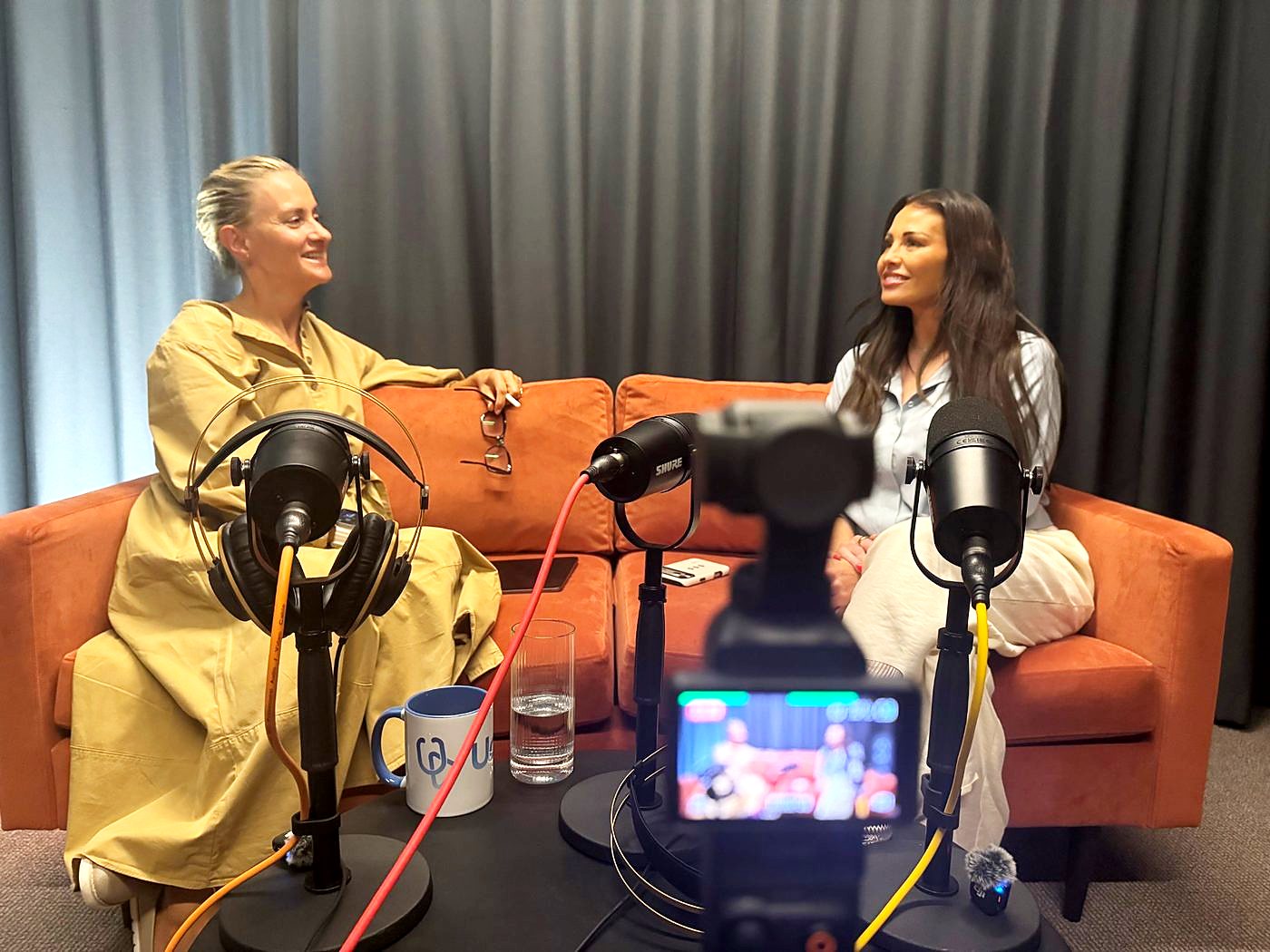 Two people in conversation on an orange sofa in The Dokkcast studio, with microphones and a camera in the foreground